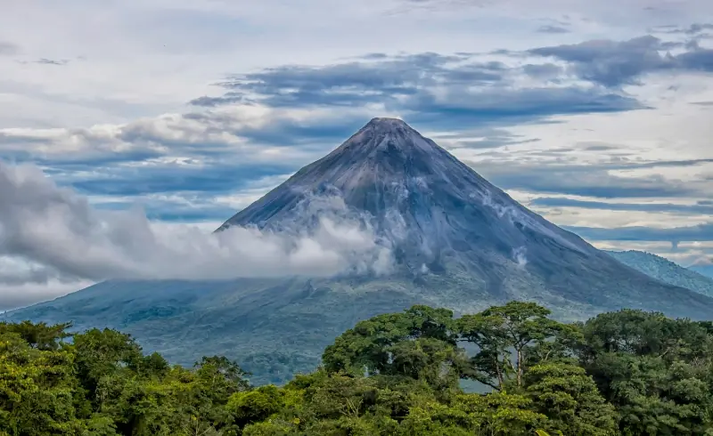 Volcán Arenal al fondo rodeado de nubes con alta vegetación por delante