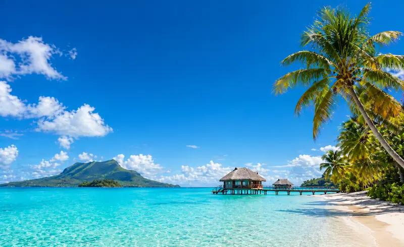 Playa paradisíaca con palmeras, bungalows sobre el agua y mar turquesa