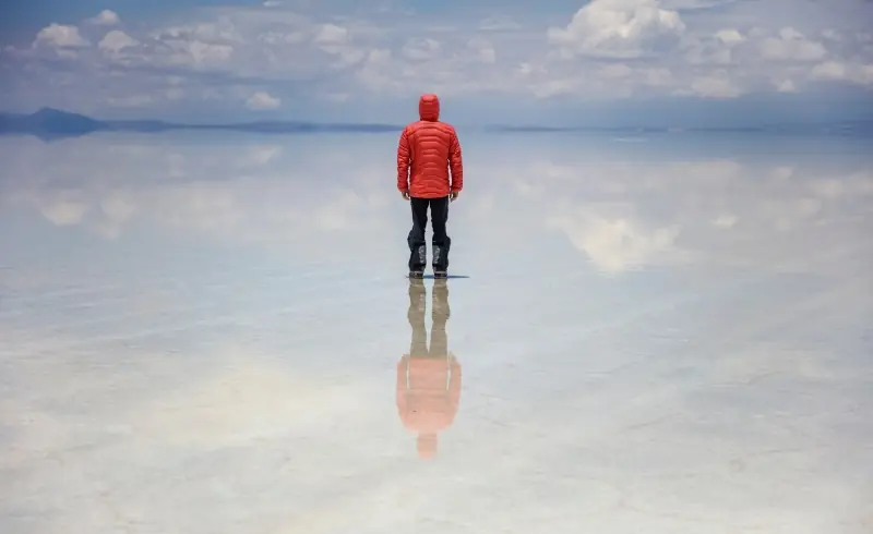 Viajero en el Salar de Uyuni con reflejo del cielo en Bolivia